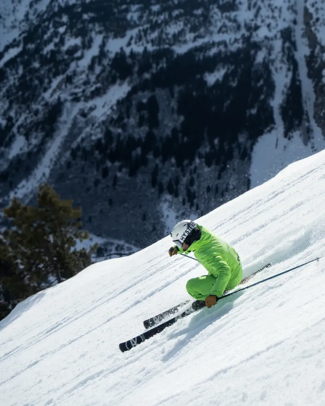 Esquiador con chaqueta verde trazando un giro en nieve polvo profunda