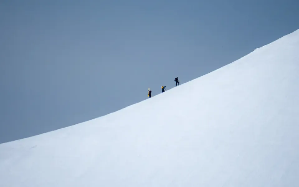 Three ski tourers climbing a snowy ridge under a pale sky