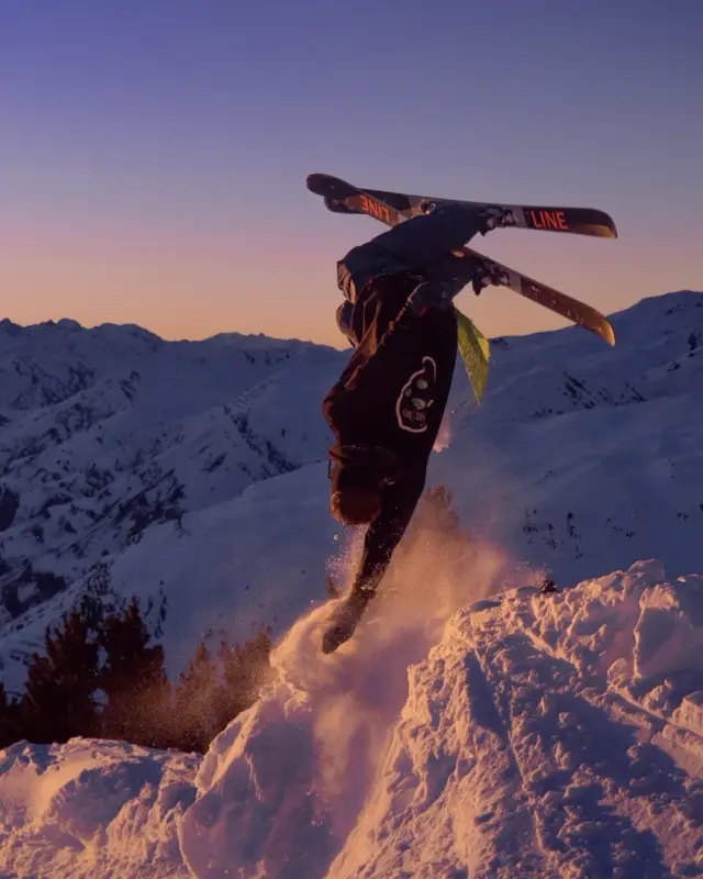 Skier doing a handstand on a snow kicker at sunset