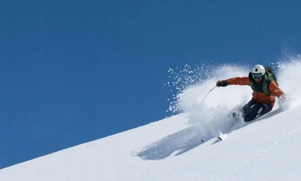 Ski instructor carving a powder turn under a blue sky
