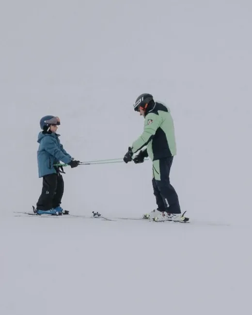 Ski instructor holding poles out to a young skier on a gentle slope